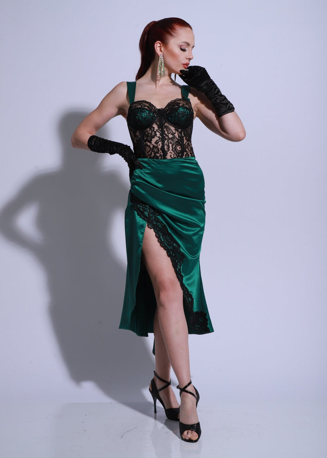 Vestido de tango verde con cuerpo de encaje, falda drapeada en satén y tajo lateral alto, modelo posando con guantes largos negros.