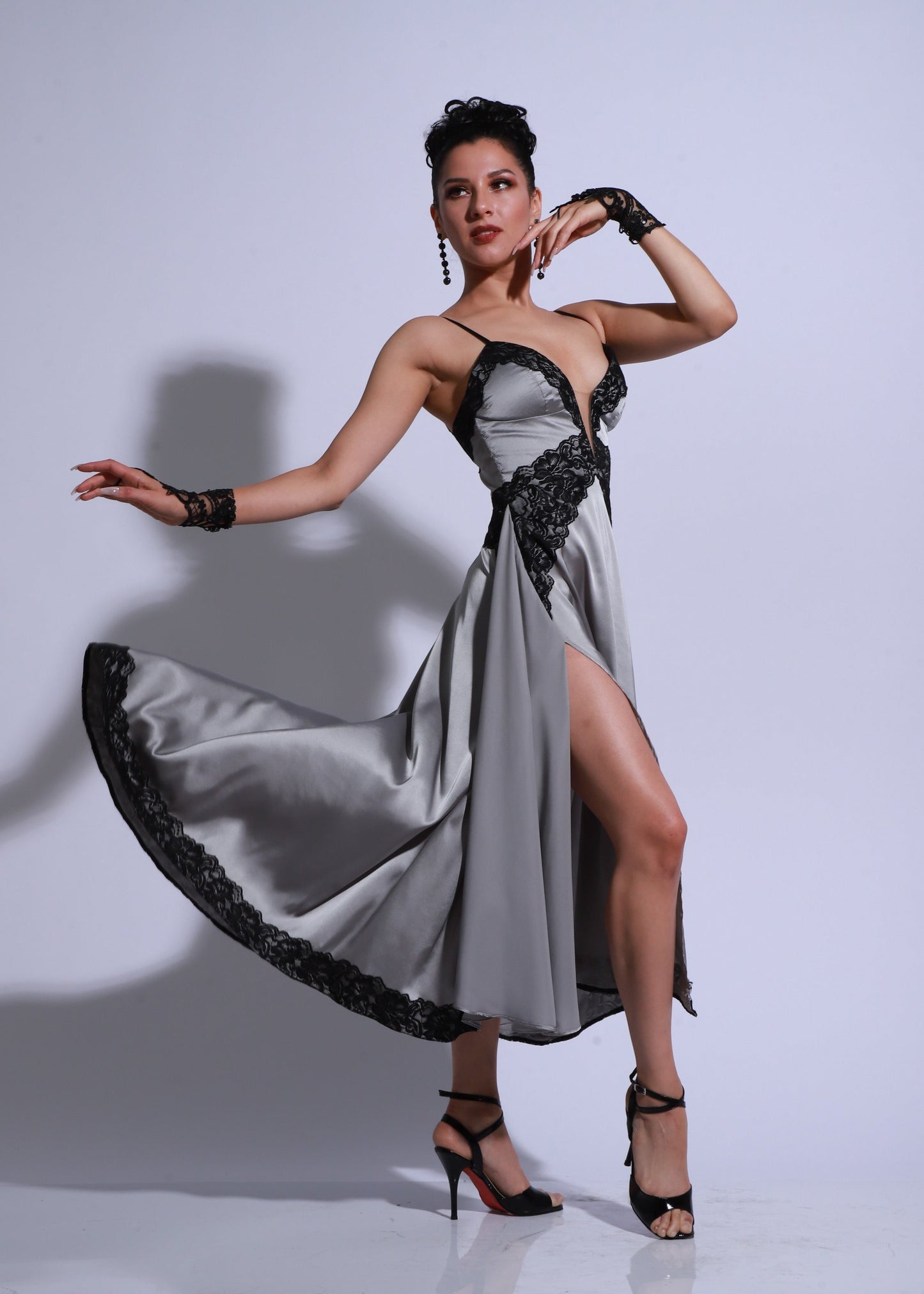 Vestido de tango gris con falda asimétrica, encaje negro y abertura lateral, modelo femenina posando con movimiento.